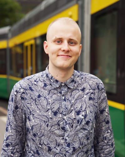 Akseli is smiling, there is a Finnish tram behind him